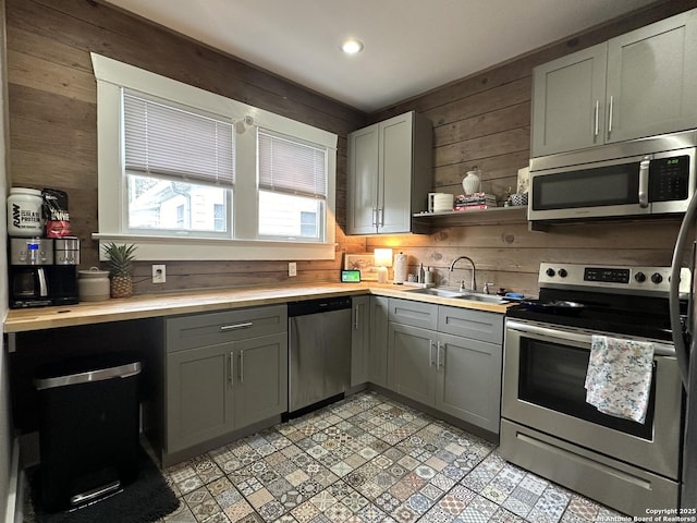 kitchen with sink, wooden walls, gray cabinetry, and appliances with stainless steel finishes