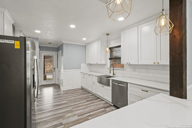 kitchen with hanging light fixtures, sink, white cabinetry, light stone countertops, and stainless steel appliances