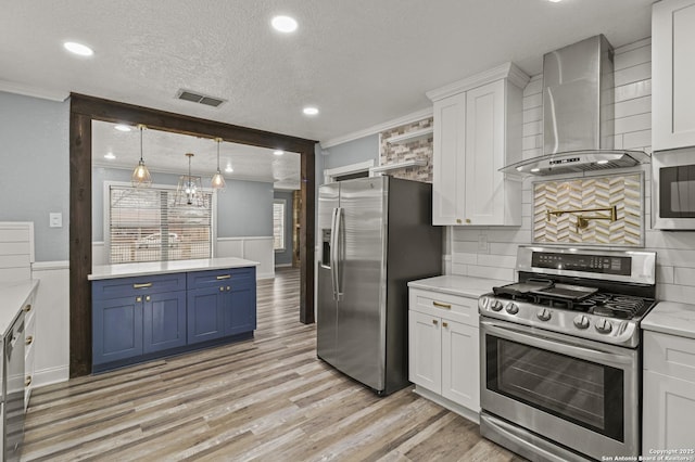 kitchen with white cabinets, wall chimney exhaust hood, stainless steel appliances, blue cabinetry, and ornamental molding