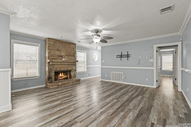 unfurnished living room featuring a stone fireplace, ornamental molding, and plenty of natural light