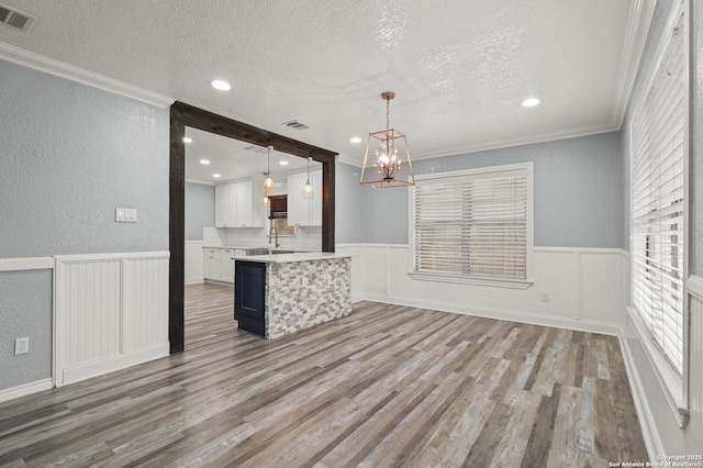 interior space with a textured ceiling, white cabinets, hardwood / wood-style floors, hanging light fixtures, and crown molding