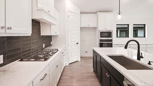 kitchen with tasteful backsplash, a sink, light wood-style floors, stainless steel appliances, and white cabinetry