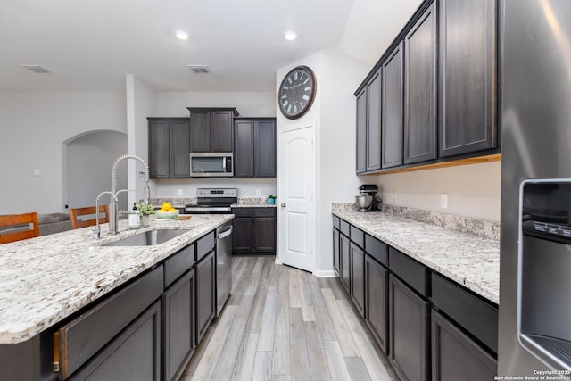 kitchen featuring appliances with stainless steel finishes, sink, a kitchen island with sink, light wood-type flooring, and light stone counters