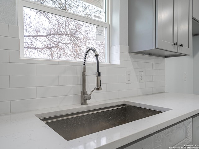 interior details with sink, backsplash, gray cabinetry, and light stone countertops