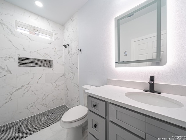 bathroom with tiled shower, vanity, and toilet