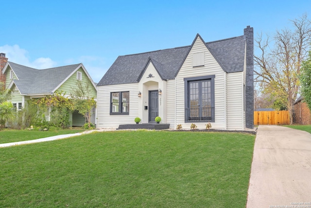 view of front of house with a shingled roof, a front yard, fence, and a chimney