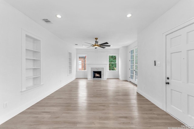 unfurnished living room featuring ceiling fan, built in features, a premium fireplace, and light wood-type flooring