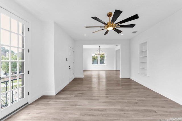 empty room featuring built in features, light wood-type flooring, and ceiling fan with notable chandelier