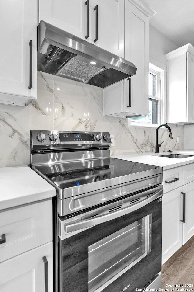 kitchen featuring white cabinetry, range hood, stainless steel electric range oven, and sink