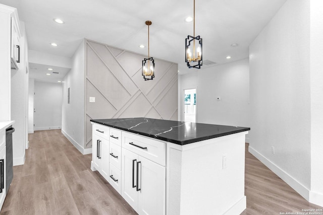 kitchen featuring white cabinets, a center island, dark stone countertops, light hardwood / wood-style floors, and hanging light fixtures