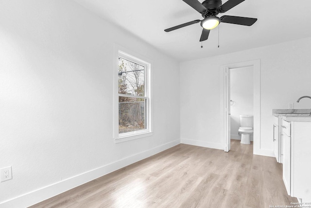 unfurnished bedroom featuring light wood-type flooring, ceiling fan, sink, and ensuite bath