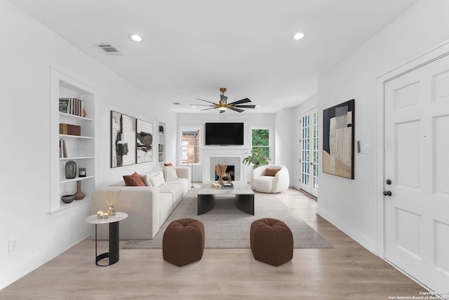 living room with built in features, ceiling fan, a high end fireplace, and light hardwood / wood-style flooring