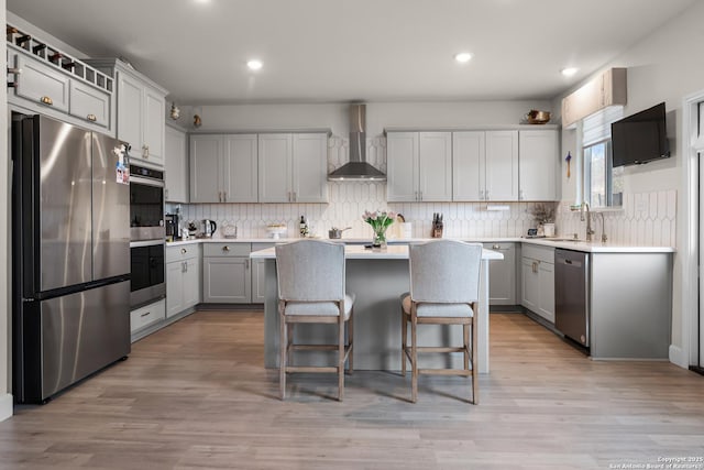 kitchen with wall chimney exhaust hood, a kitchen island, a kitchen breakfast bar, and appliances with stainless steel finishes