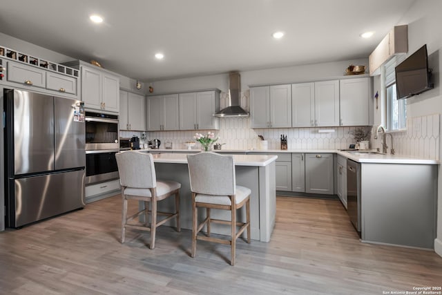 kitchen featuring wall chimney exhaust hood, light wood-type flooring, a center island, a breakfast bar area, and stainless steel appliances