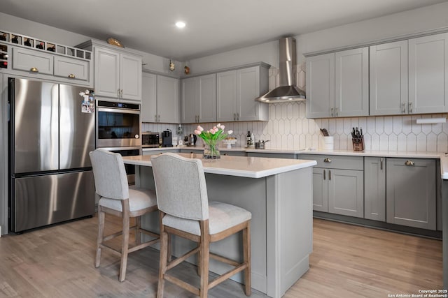 kitchen with wall chimney exhaust hood, gray cabinets, a kitchen breakfast bar, and stainless steel appliances