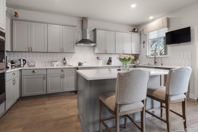 kitchen with wall chimney range hood, gray cabinets, a breakfast bar area, and a kitchen island