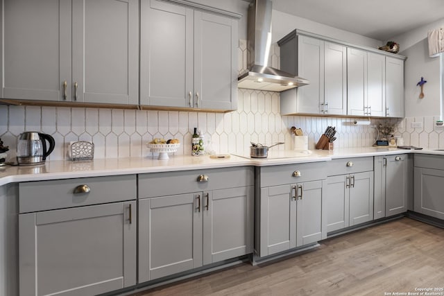 kitchen featuring gray cabinets, backsplash, wall chimney range hood, and light hardwood / wood-style floors