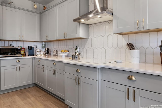 kitchen with exhaust hood, light hardwood / wood-style floors, backsplash, electric cooktop, and gray cabinetry