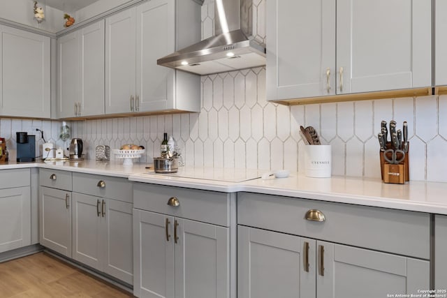 kitchen featuring light hardwood / wood-style floors, electric stovetop, wall chimney range hood, backsplash, and gray cabinets