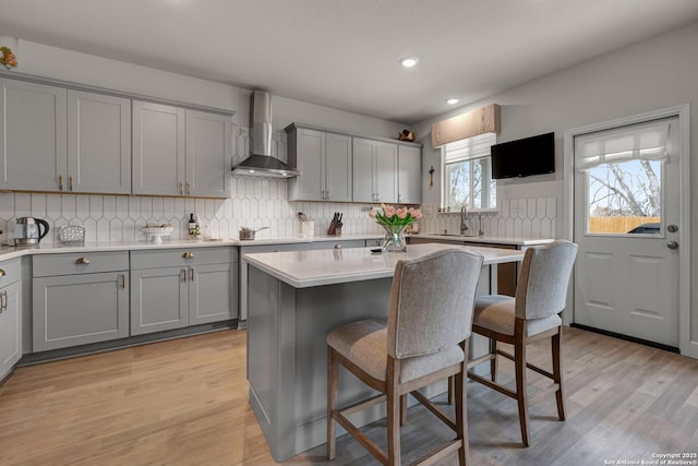 kitchen with a center island, light hardwood / wood-style flooring, wall chimney exhaust hood, and gray cabinetry