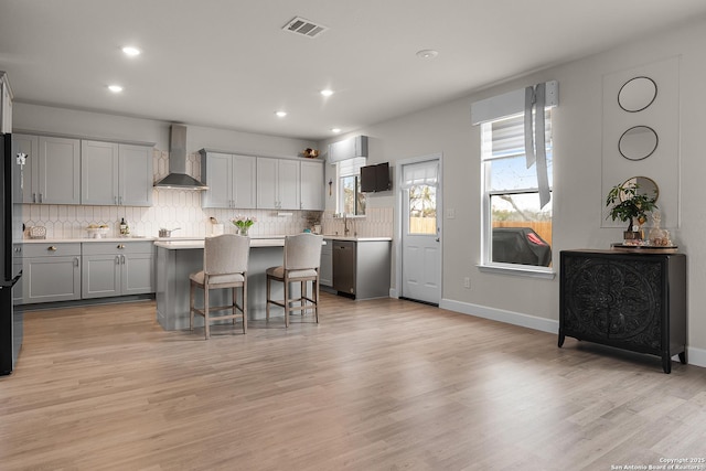 kitchen with wall chimney exhaust hood, light wood-type flooring, a center island, and a kitchen breakfast bar