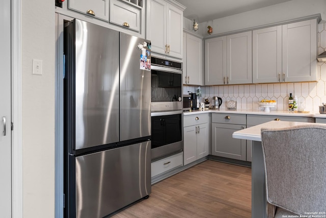 kitchen featuring light wood-type flooring, backsplash, appliances with stainless steel finishes, and gray cabinetry