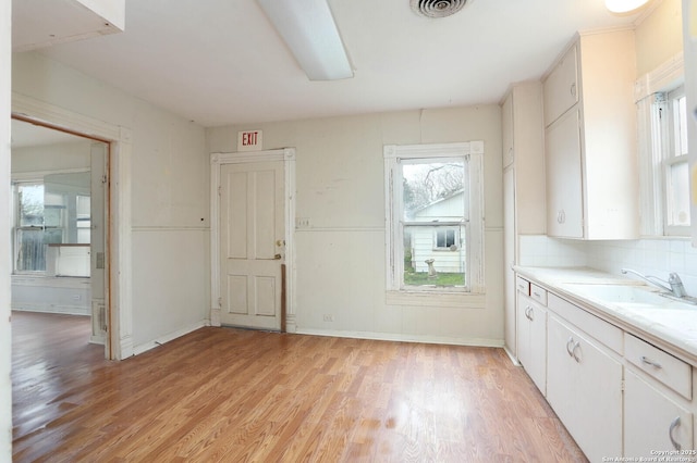 interior space featuring sink, light wood-type flooring, white cabinetry, and tasteful backsplash