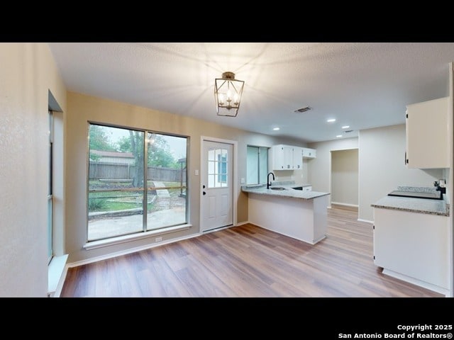 kitchen featuring kitchen peninsula, sink, white cabinets, light wood-type flooring, and an inviting chandelier