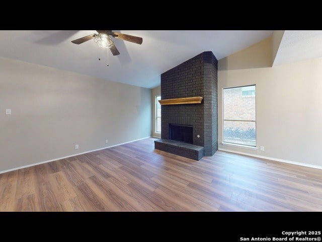 unfurnished living room featuring plenty of natural light, hardwood / wood-style flooring, vaulted ceiling, and a brick fireplace