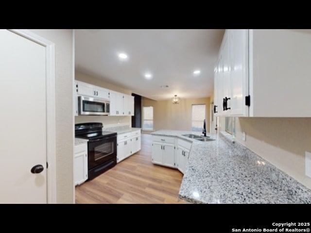 kitchen with light stone countertops, white cabinets, sink, electric range, and kitchen peninsula