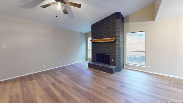 unfurnished living room with vaulted ceiling, a brick fireplace, a healthy amount of sunlight, and hardwood / wood-style floors