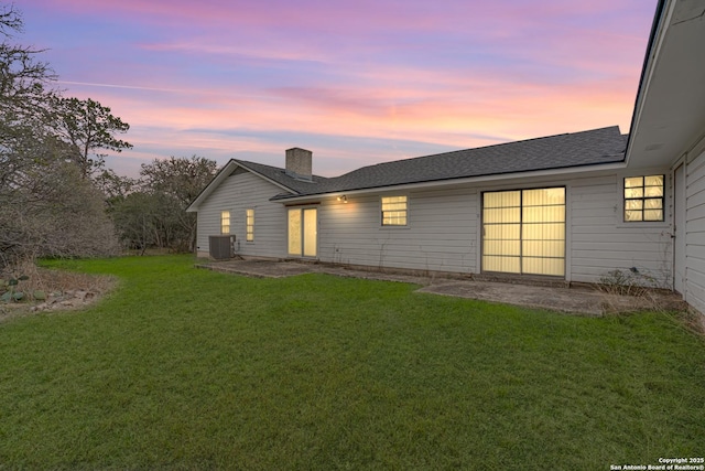 back house at dusk with central AC, a patio, and a yard