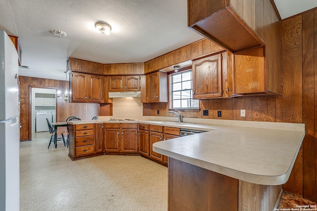 kitchen with washer and dryer, white appliances, sink, wood walls, and kitchen peninsula