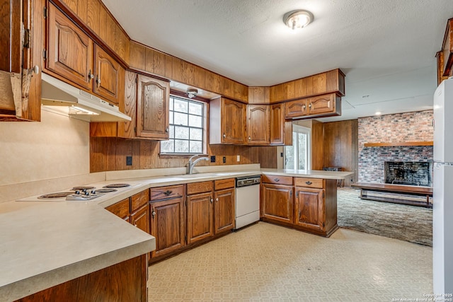 kitchen featuring white appliances, light carpet, sink, kitchen peninsula, and a brick fireplace