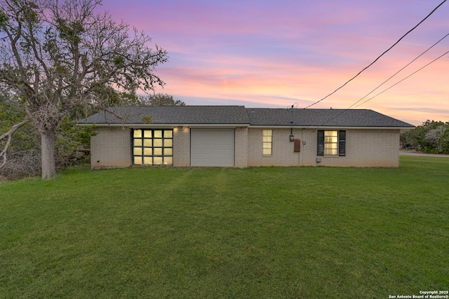 back house at dusk featuring a lawn and a garage