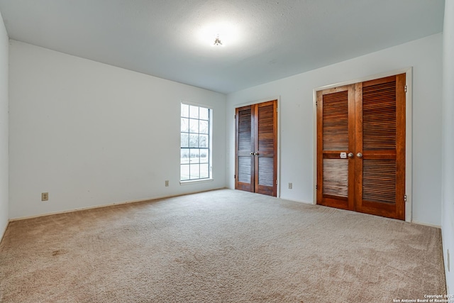 unfurnished bedroom with carpet flooring, two closets, and french doors