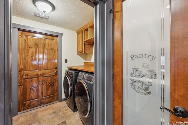 washroom with cabinets, washing machine and dryer, and a textured ceiling