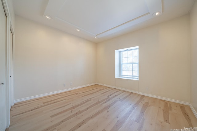 empty room featuring a tray ceiling and light hardwood / wood-style flooring