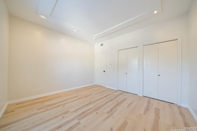 unfurnished bedroom with two closets and light wood-type flooring