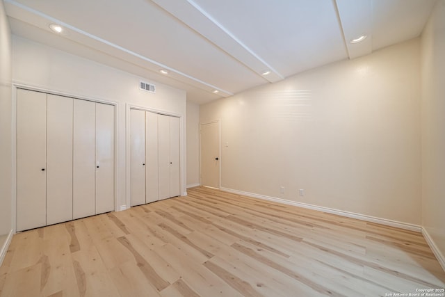 unfurnished bedroom with light hardwood / wood-style floors and two closets