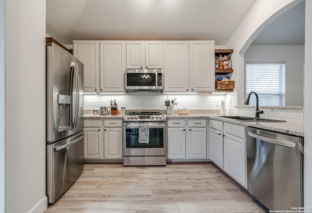 kitchen with sink, backsplash, white cabinets, light stone countertops, and stainless steel appliances