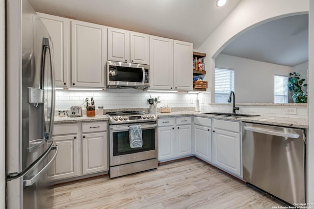 kitchen featuring vaulted ceiling, sink, white cabinets, decorative backsplash, and stainless steel appliances