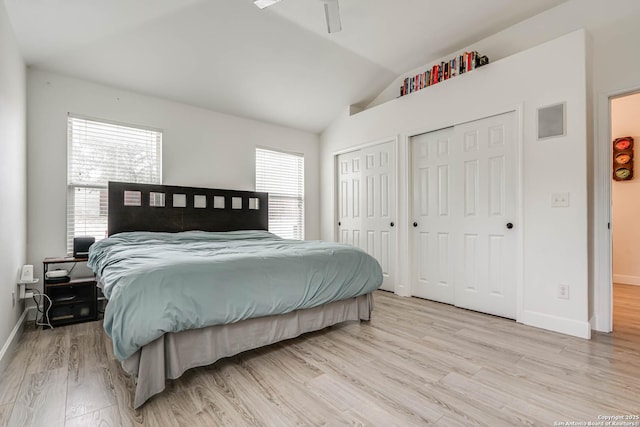 bedroom with light hardwood / wood-style floors, vaulted ceiling, and two closets