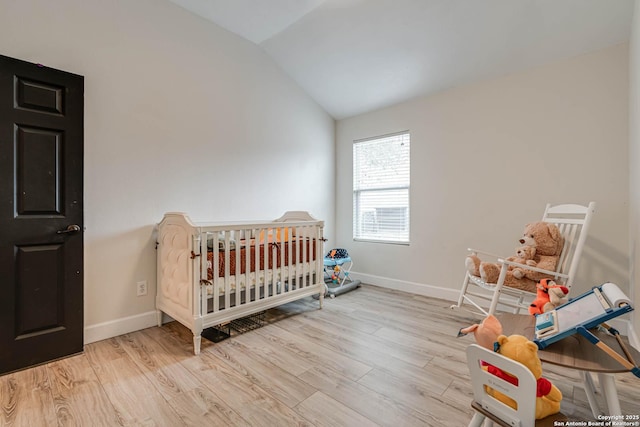 bedroom with vaulted ceiling, a nursery area, and light hardwood / wood-style floors