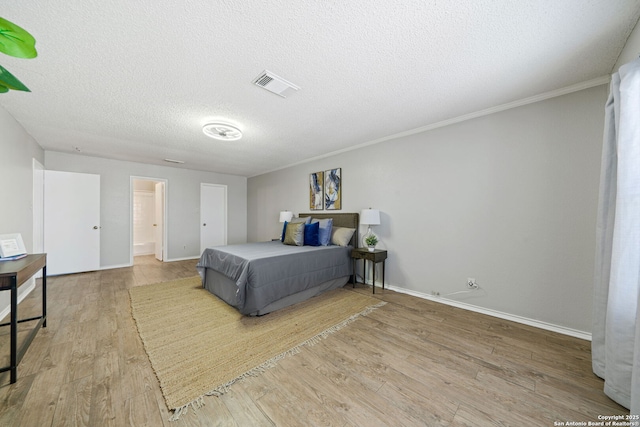 bedroom featuring light hardwood / wood-style floors, ensuite bath, a textured ceiling, and crown molding