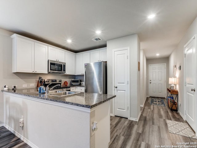 kitchen featuring hardwood / wood-style floors, appliances with stainless steel finishes, white cabinetry, sink, and kitchen peninsula