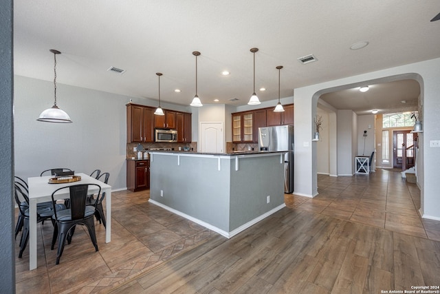 kitchen with hanging light fixtures, appliances with stainless steel finishes, backsplash, a center island, and dark hardwood / wood-style floors