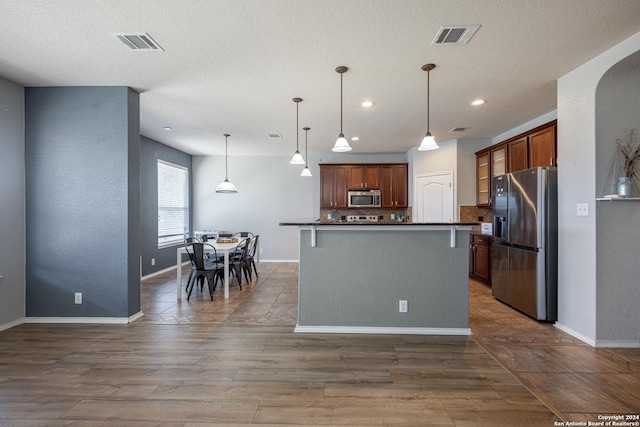 kitchen with stainless steel appliances, a kitchen island, hanging light fixtures, and dark hardwood / wood-style flooring