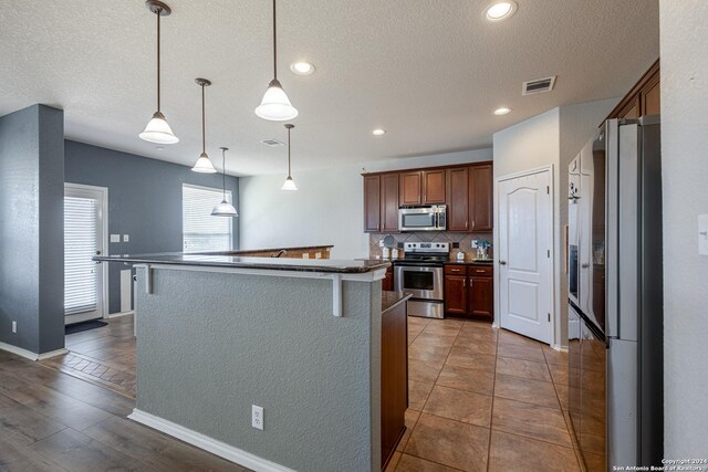 kitchen with hanging light fixtures, a center island with sink, appliances with stainless steel finishes, and tasteful backsplash