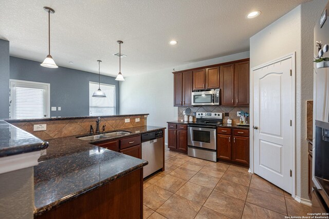 kitchen featuring pendant lighting, sink, dark stone countertops, decorative backsplash, and stainless steel appliances